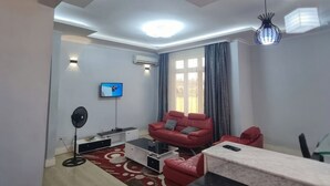 A modern living room with a red sofa, a TV, and a fan.