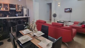 A modern living room with a dining area, red sofas, a TV, and a kitchen with marble countertops.