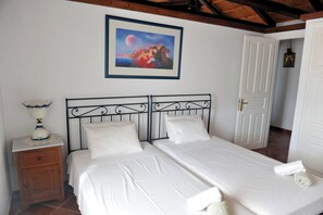 A bedroom with two beds, a nightstand, a framed picture on the wall, and a door leading to another room. - VILLA ATHINA (Hydra)