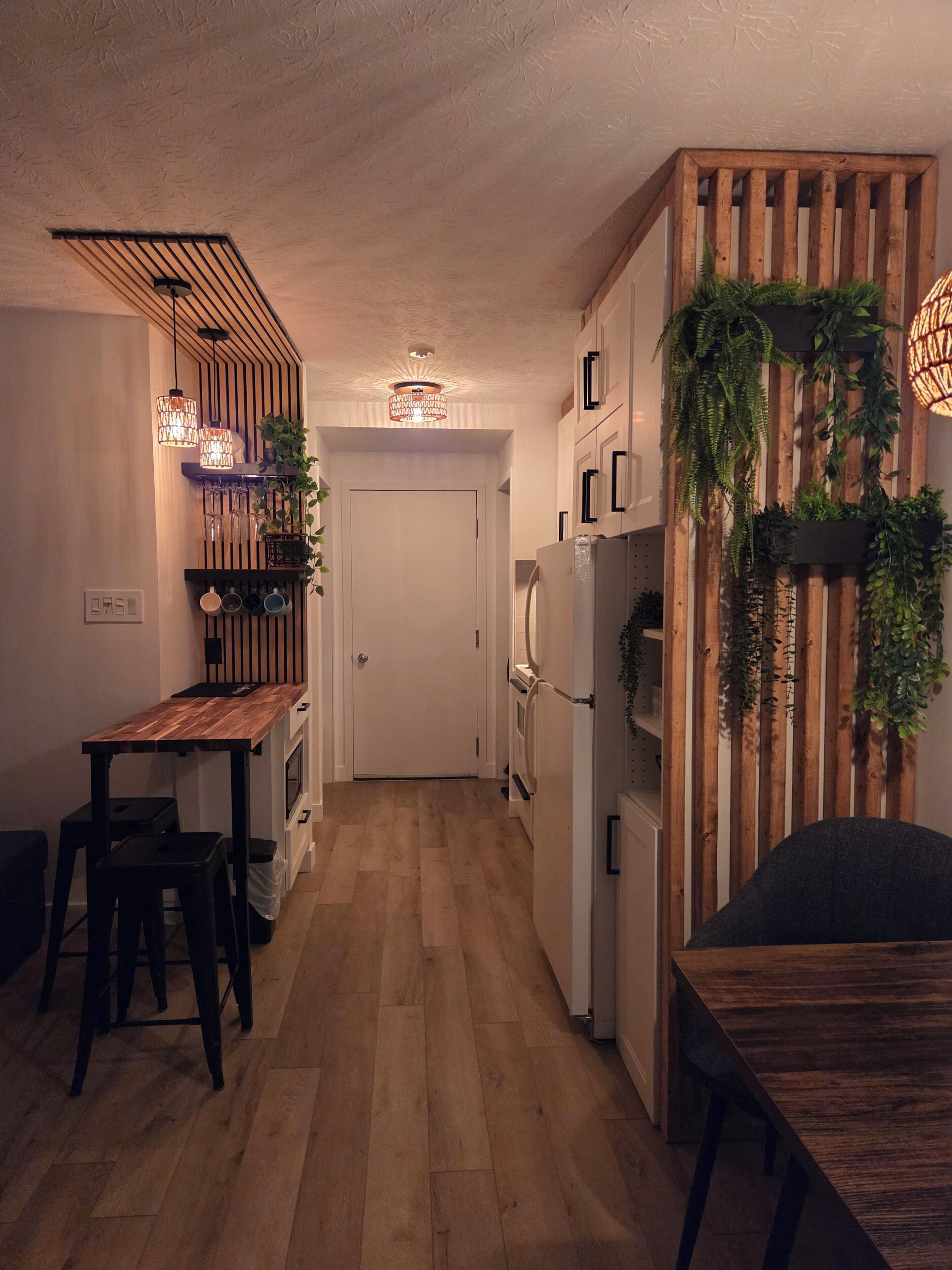 Eine Küche mit Holzboden, einem Esstisch, Barhocker, Pendelleuchten und einem Kühlschrank.