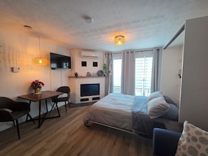 Ein Schlafzimmer mit Bett, Schreibtisch, Fernseher, Kamin und einem Balkon.