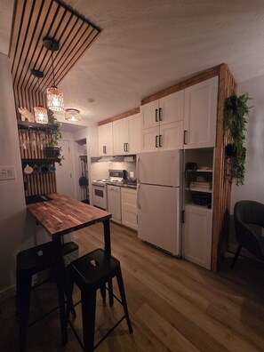 Eine Küche mit Holzboden, weißen Schränken, einem Esstisch aus Holz mit zwei Stühlen und hängenden Pendelleuchten.