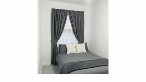 Ein Schlafzimmer mit einem Bett, grauen Vorhängen und weißen Wänden.