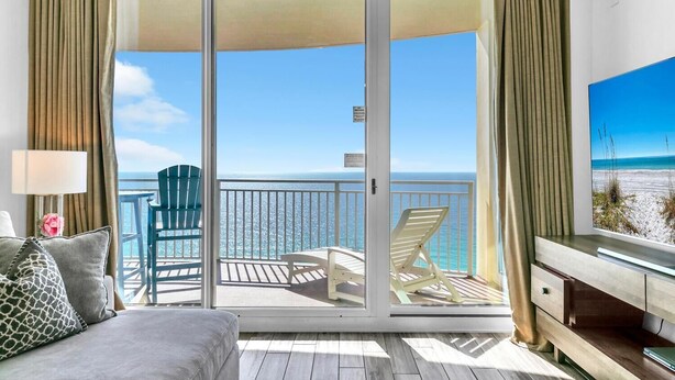 A balcony with a view of the ocean, a sofa, a chair, and a TV on a stand. - Aqua Resort 2003 (Panama City Beach)