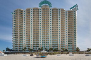 Ein Hochhaus-Hotel mit mehreren Balkonen, einer Strandlage und einer kleinen Strandhütte.
