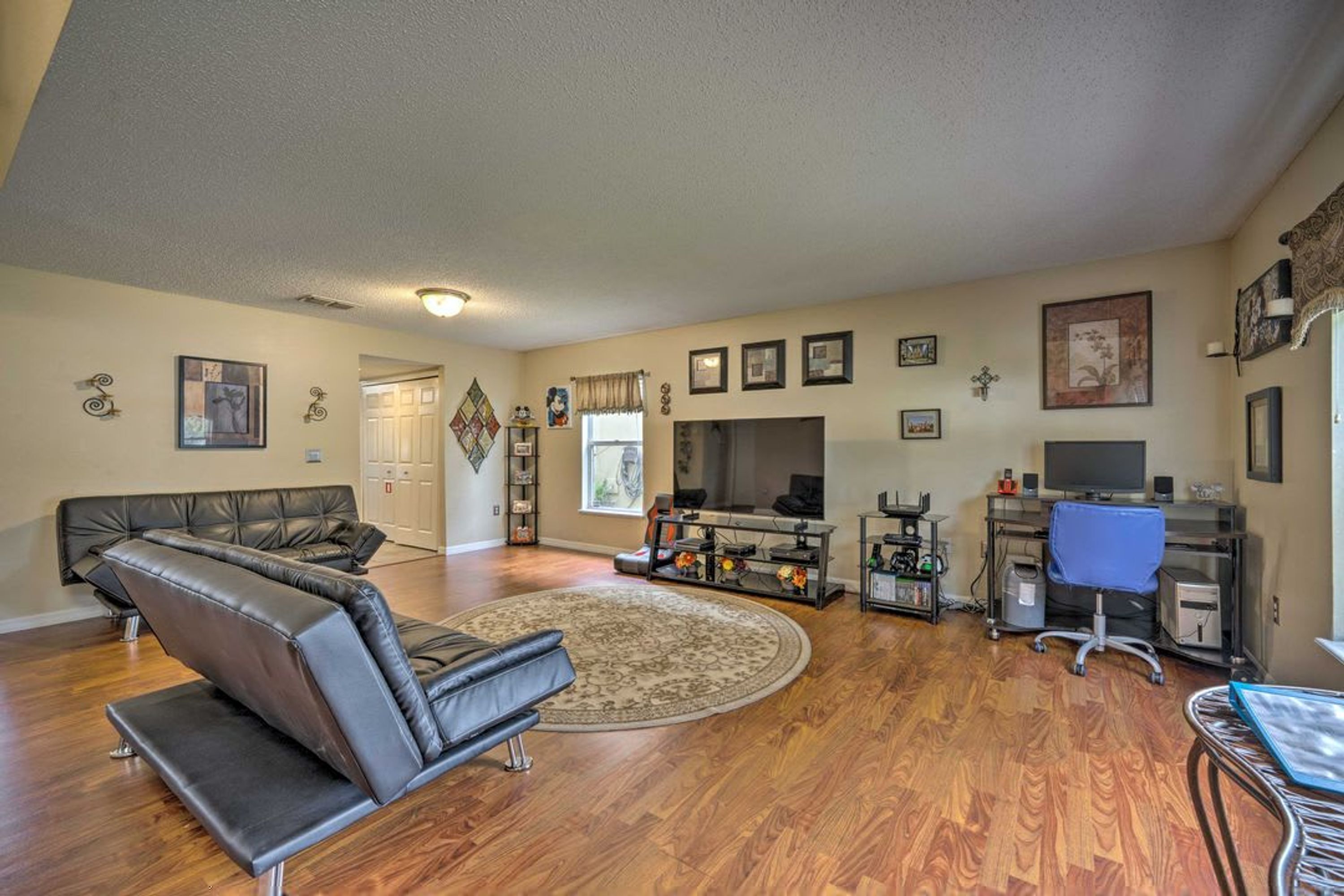 A spacious living room with a leather sofa, a TV, and a computer desk.