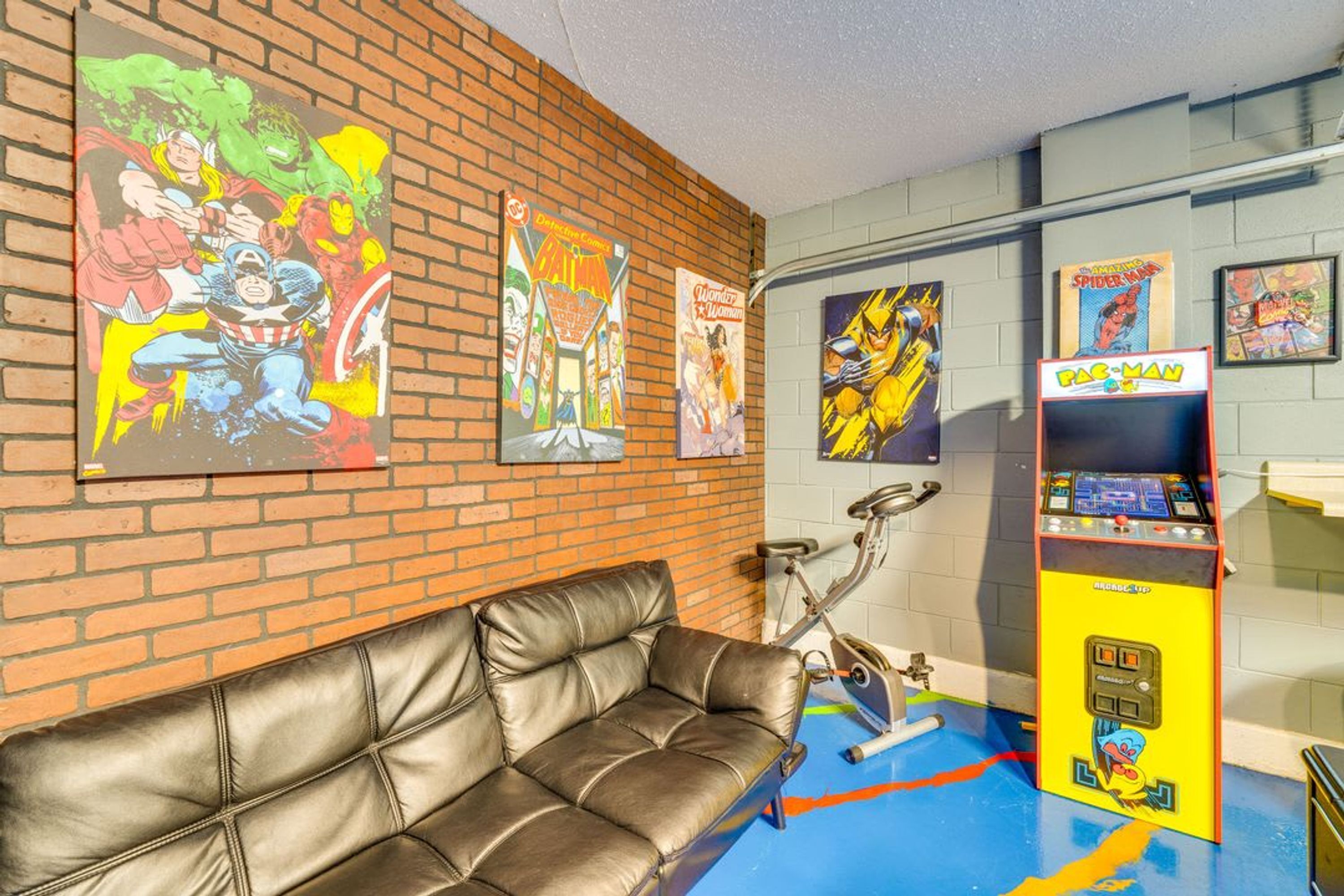 Ein Zimmer mit Backsteinwand, einem Ledersofa und einem farbenfrohen Spielautomaten.