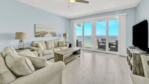 A living room with a sofa, coffee table, TV, and a balcony with a view of the ocean. - Blue Skies and Gulf Breezes! Enjoy Blue Serenity at LTW Nice Gulf View balcony (Panama City Beach)