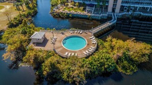 An aerial view of a resort with a circular pool surrounded by a wooden deck, a bridge, and lush greenery. - Blue Skies and Gulf Breezes! Enjoy Blue Serenity at LTW Nice Gulf View balcony (Panama City Beach)