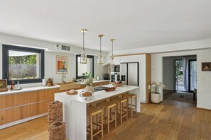 Una cocina moderna con una isla central, taburetes de madera, luces colgantes y un amplio ventanal.