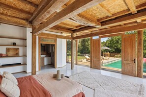 A spacious bedroom with a large bed, wooden ceiling beams, a view of a swimming pool, and a sliding glass door leading to an outdoor area. - Chic and spacious Balinese-style villa - peaceful and quiet, close to Aix-en-Pce (Saint-Marc-Jaumegarde)