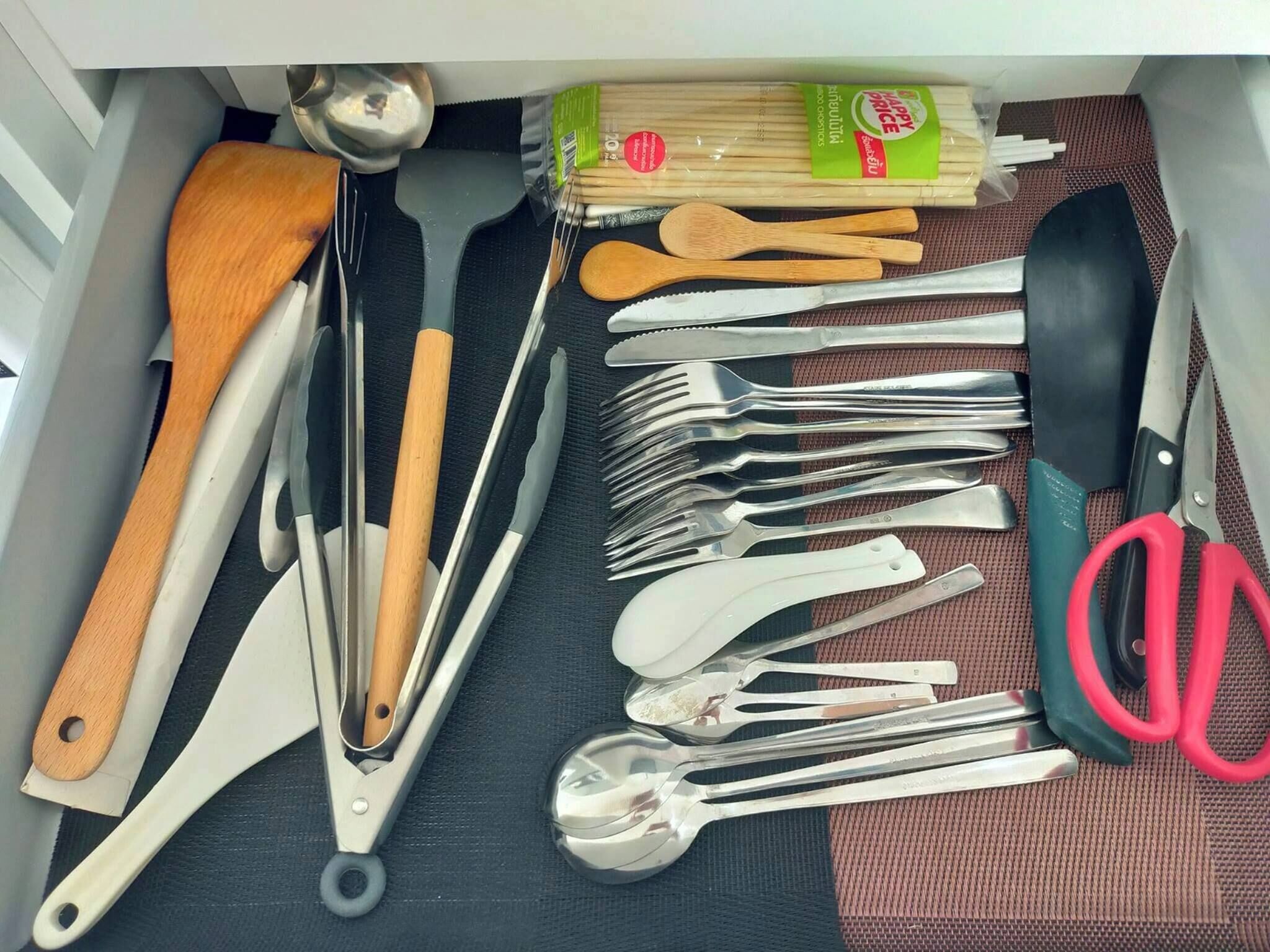 A drawer containing various kitchen utensils including spoons, forks, a spatula, and a pair of scissors.