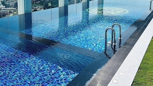 An infinity pool with clear blue water, surrounded by a white colonnade, and offering a view of the cityscape. - 2 Bed Room Sea View Great Place 2 (Pattaya)