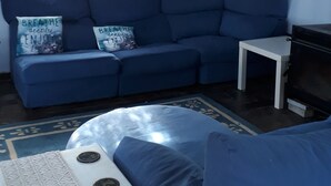 Een woonkamer met een blauwe bank, een witte bijzettafeltje en een decoratief wandobject.