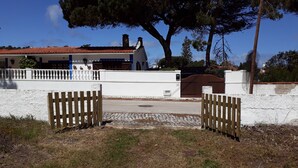 Een hekwerk poort met een verharde oprit die leidt naar een wit gebouw met een rood dak.