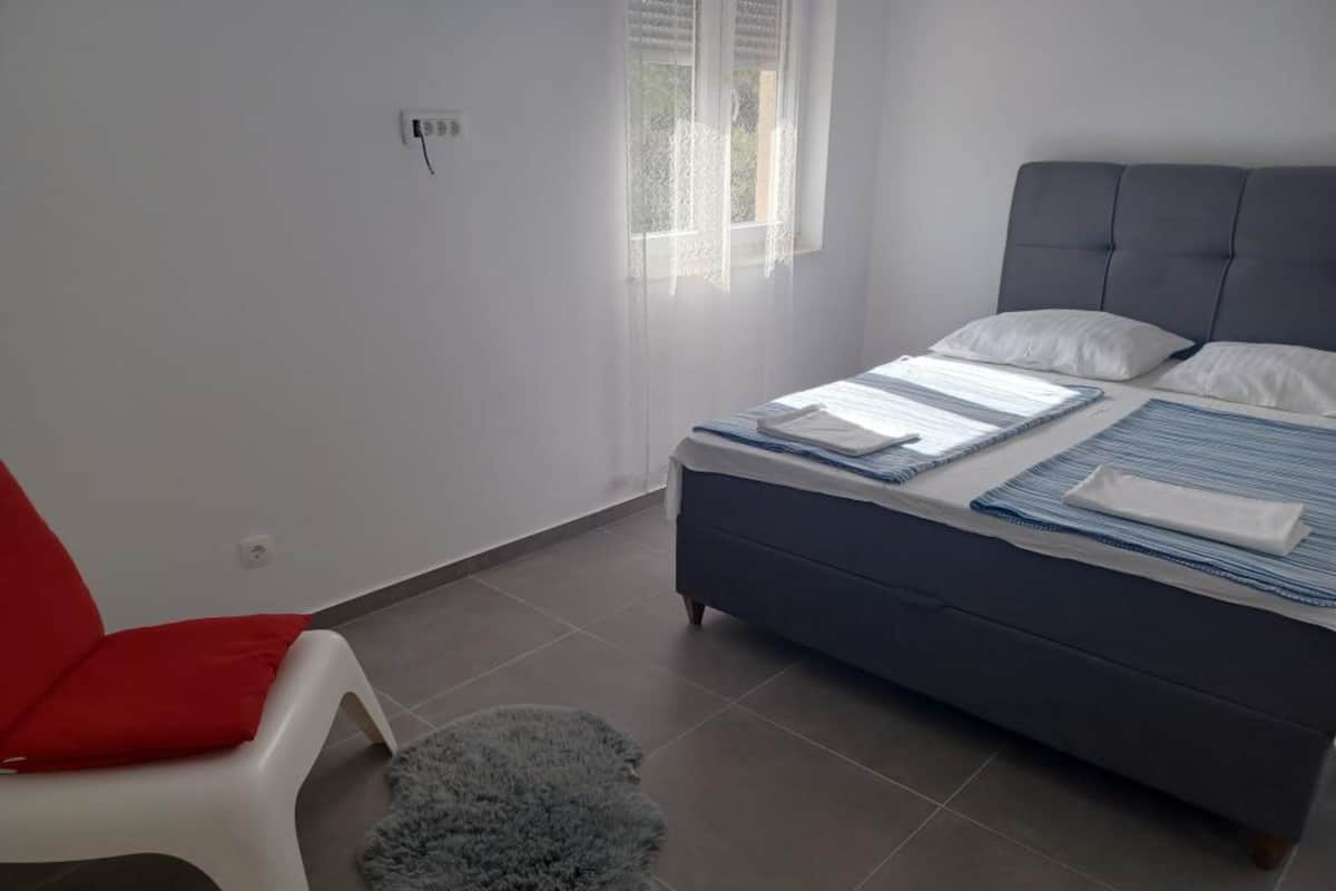 Een slaapkamer met een bed, een rode stoel en een pluizig vloerkleed.