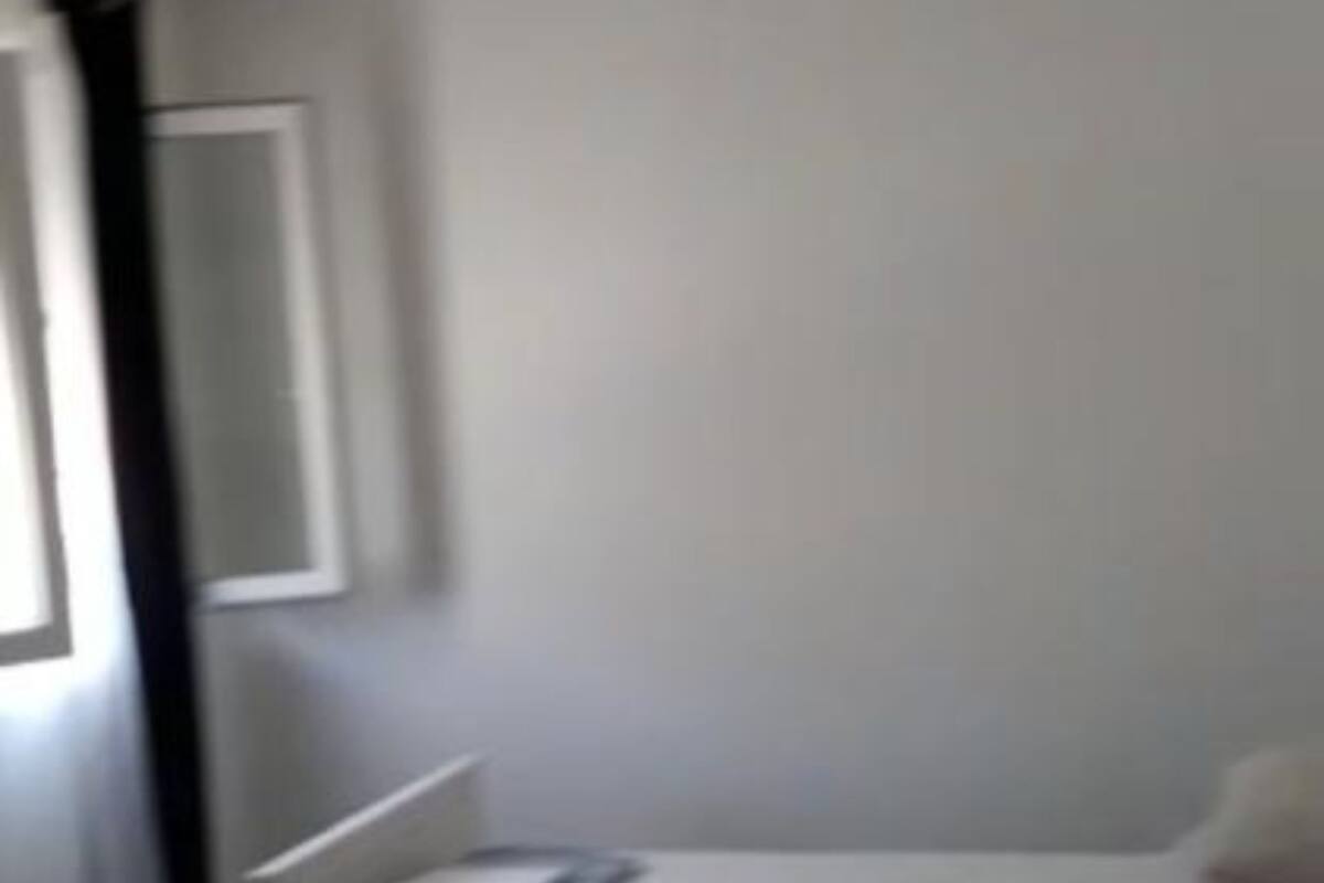 Een kamer met een bed, een raam met gordijnen en een wandlamp.