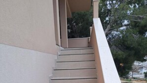 Eine Treppe in Beige führt zu einem Balkon mit Blick auf Bäume und einen Zaun.