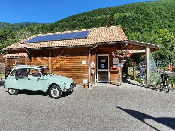 A wooden building with a solar panel, a vintage car, and a bicycle.