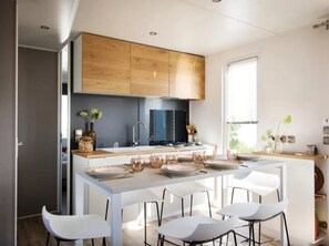 A modern kitchen with wooden cabinets, a central island with seating, and a large window providing natural light.
