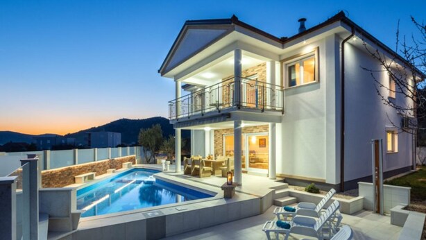 Une maison à deux étages avec une piscine, un espace salon extérieur et un balcon.