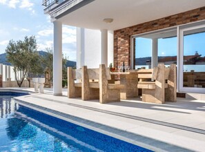 A poolside area with a table and chairs, a brick wall, and a view of the mountains. - Guest House Matana Pomena National Park (Mljet)