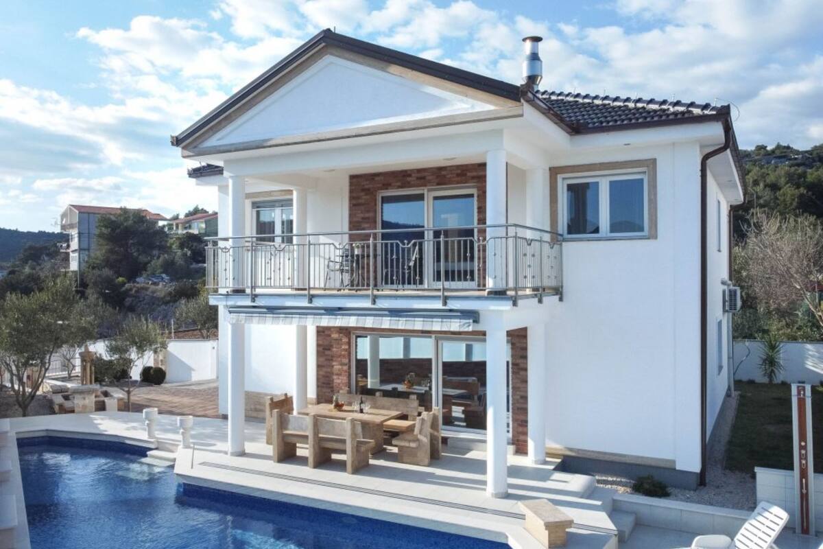 Una casa de dos pisos con balcón, piscina y patio amoblado.