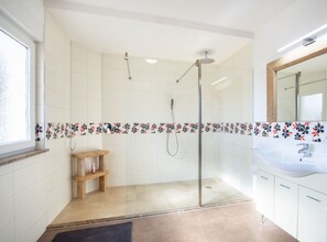 Et moderne badeværelse med en brusekabine med glasvægge, en træhylde og en hvid vask med spejl.