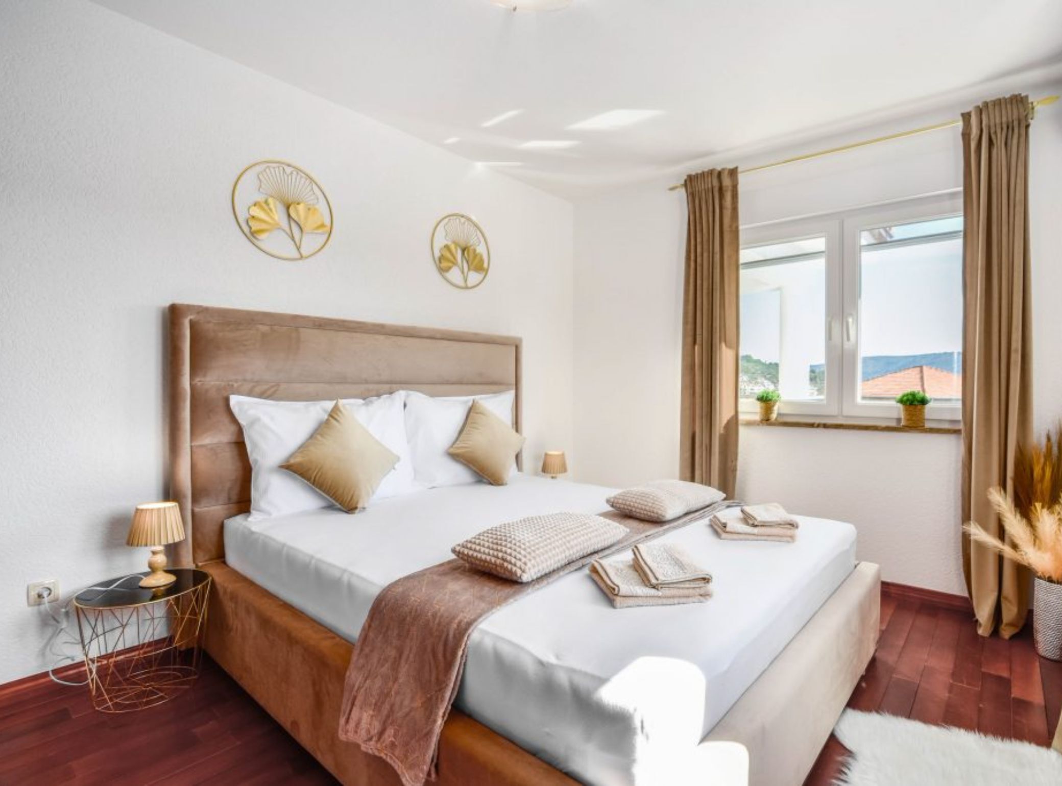 A bedroom with a large bed, a bedside table, a window with curtains, and a view of the outside.