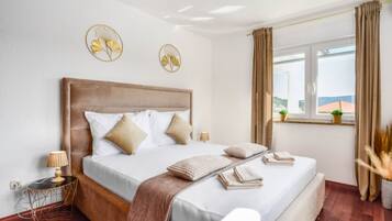 A bedroom with a large bed, a bedside table, a window with curtains, and a view of the outside.