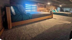 Une chambre confortable située dans les combles, avec un lit en bois, un sol recouvert d’une moquette et un ventilateur.