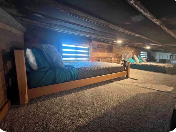 A cozy attic bedroom with a wooden bed, a carpeted floor, and a fan.