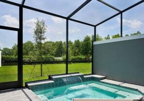 A glass-enclosed hot tub with a waterfall feature, surrounded by a grassy area and trees. - 4BD Disney Inspired Retreat with Pool Near Disney (Kissimmee)