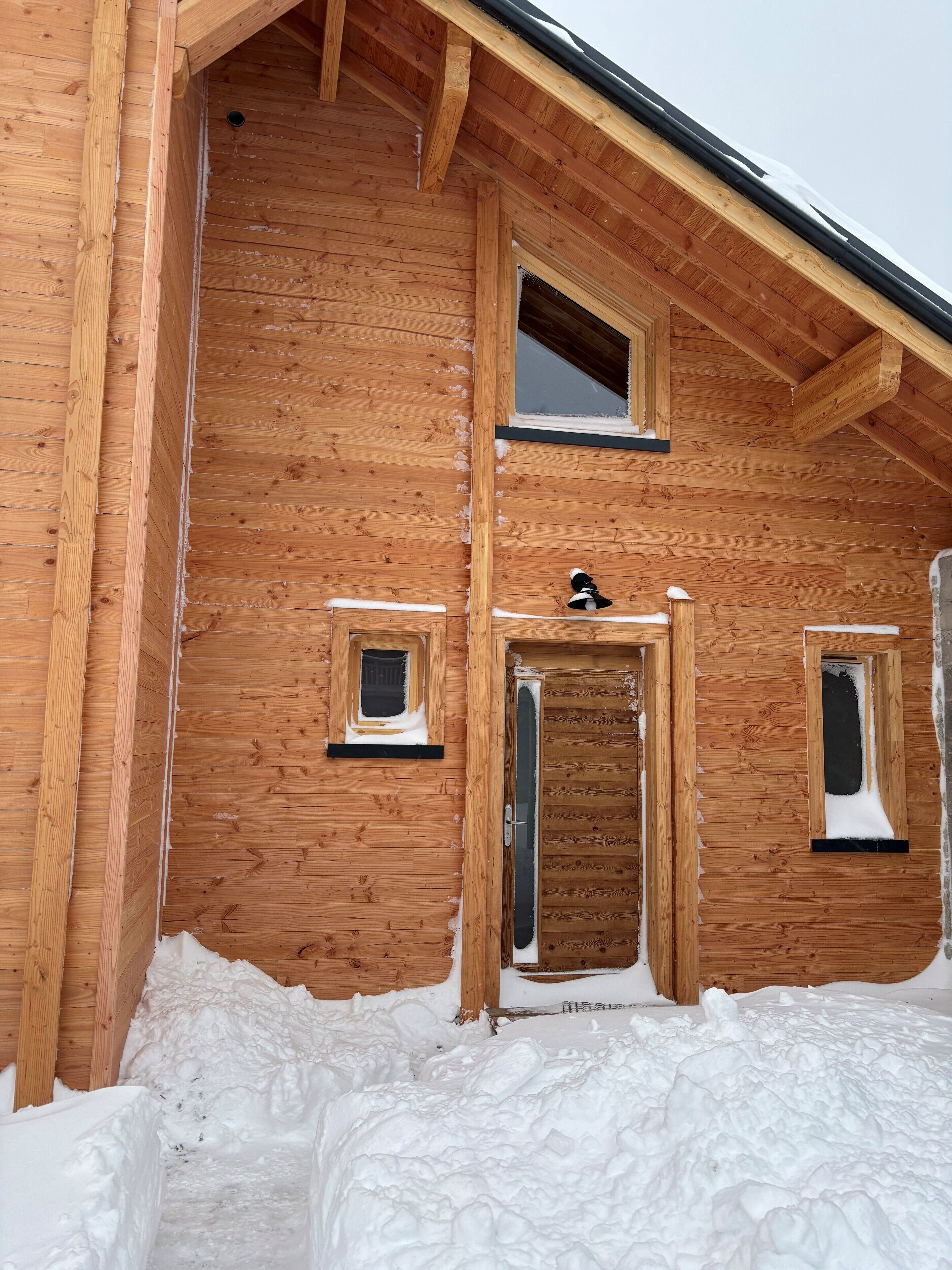 Una cabaña de madera con una entrada cubierta de nieve y dos ventanas pequeñas.