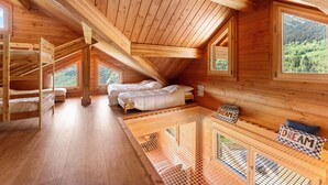 A wooden cabin with bunk beds, a loft bed, and a view of the forest.