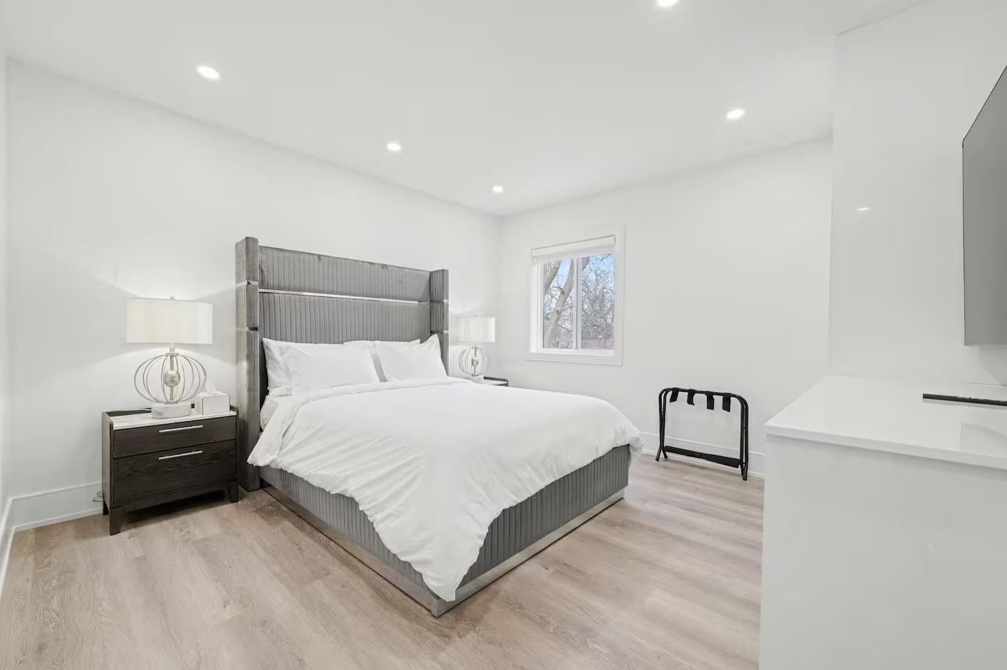 Un dormitorio moderno con cama, mesitas de noche, un ventanal y televisor.