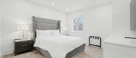 A modern bedroom with a bed, bedside tables, a nightstand, a window, and a TV.