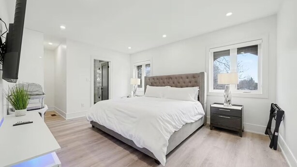 A modern bedroom with a large bed, bedside tables, a desk with a lamp, and a window. - Five-Star Comfort in a luxury Home (Brampton)