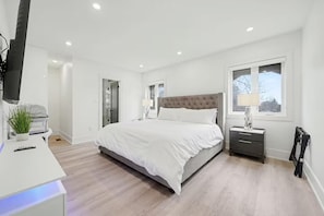 A modern bedroom with a large bed, bedside tables, a desk with a lamp, and a window. - Five-Star Comfort in a luxury Home (Brampton)