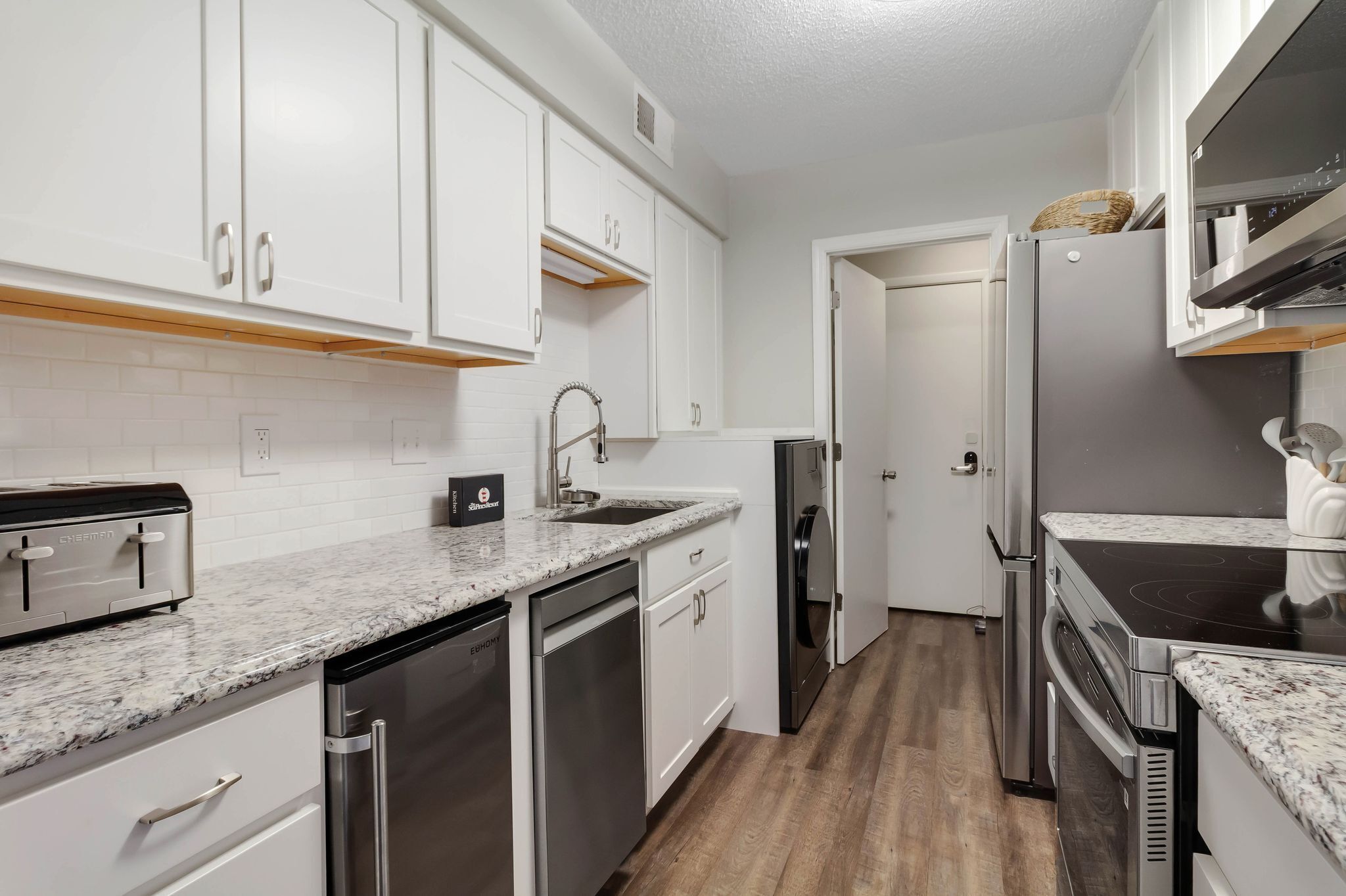 A modern kitchen with white cabinets, stainless steel appliances, a granite countertop, and a wooden floor.