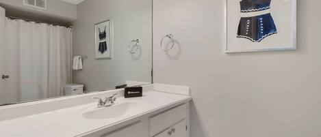 A modern bathroom with a large mirror, white vanity, and a framed artwork of a dress on the wall.