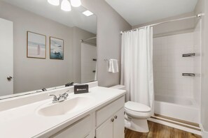 Een moderne badkamer met een wit wastafel, toilet en douche. Er hangen foto's in lijsten aan de muur en een handdoekrek.