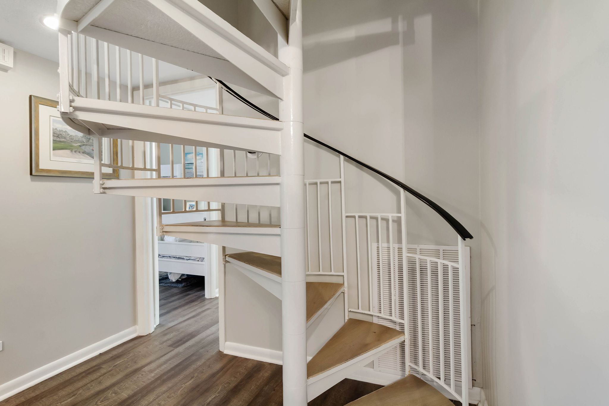 A white spiral staircase with a black handrail, wooden steps, and a white railing.