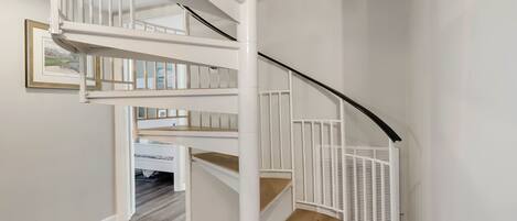 A white spiral staircase with a black handrail, wooden steps, and a white railing.