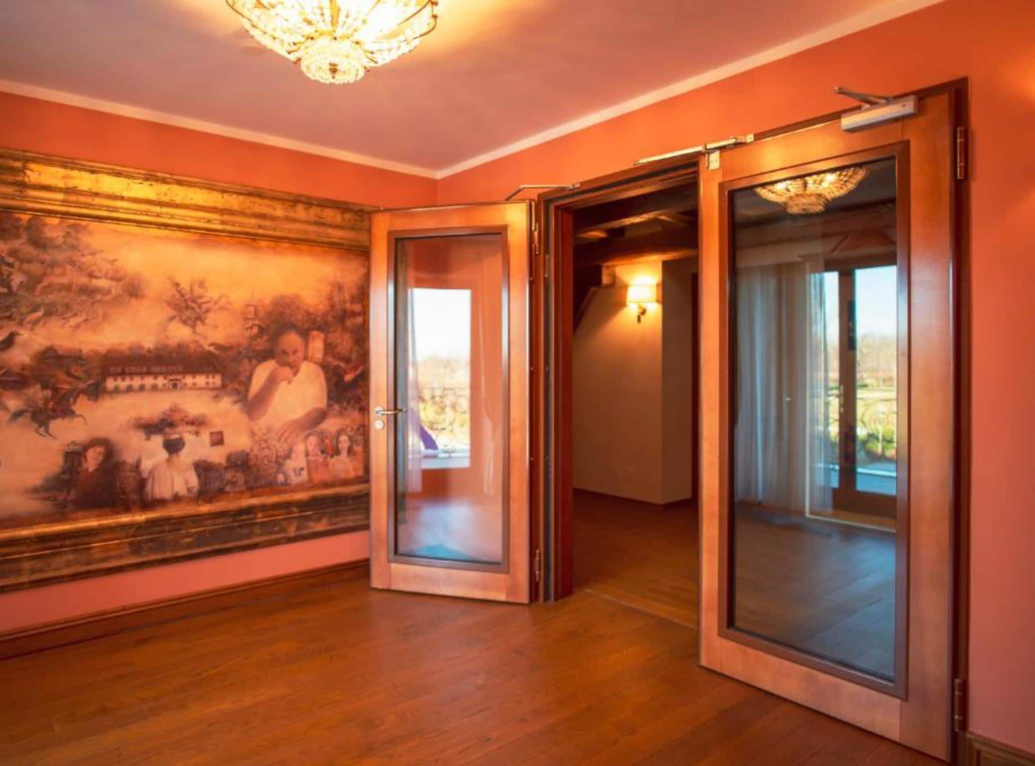 A room with a large mural, wooden flooring, and a chandelier.