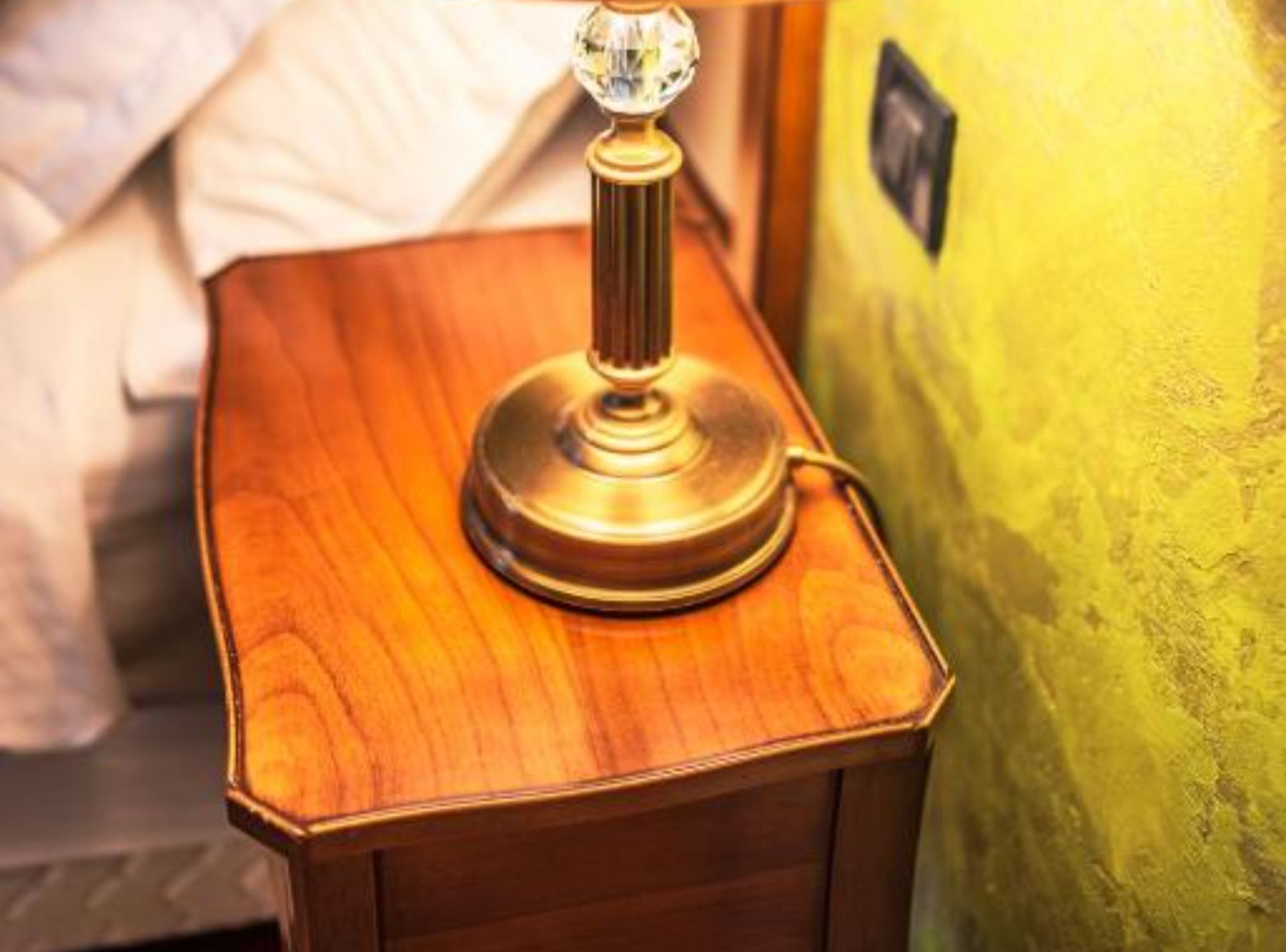 A wooden bedside table with a brass lamp featuring a crystal base.