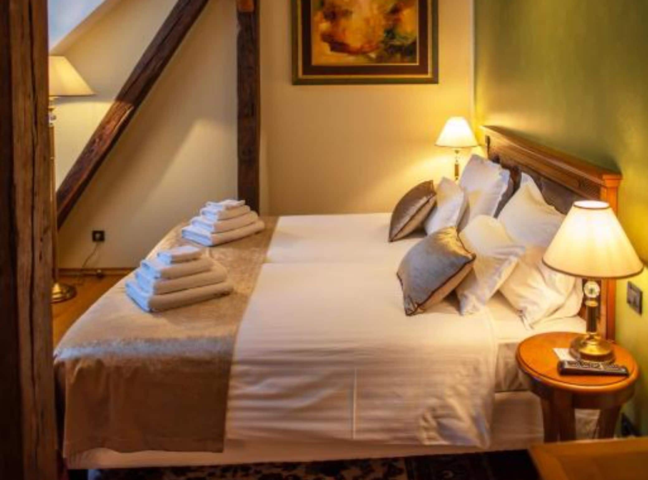 A neatly made bed with pillows and a folded blanket, a bedside lamp, and a painting on the wall.