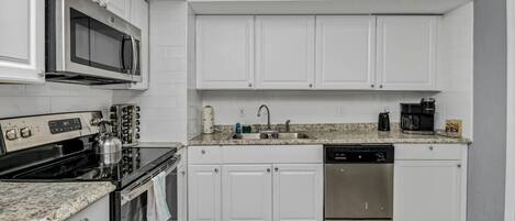 A modern kitchen with white cabinets, a stainless steel stove, a microwave, a sink, a coffee maker, and a dishwasher.