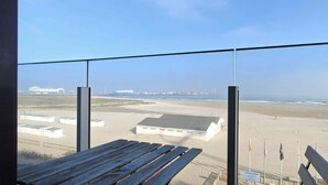 A balcony with a view of a beach, a sandy area with buildings, and a clear sky. - Beachfront Studio w/Balcony & Family Amenities (Knokke-Heist)