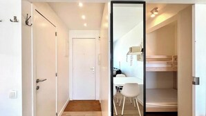 A narrow hallway with a white door, a white table with chairs, and a bunk bed in a room with white walls and wooden flooring. - Beachfront Studio w/Balcony & Family Amenities (Knokke-Heist)